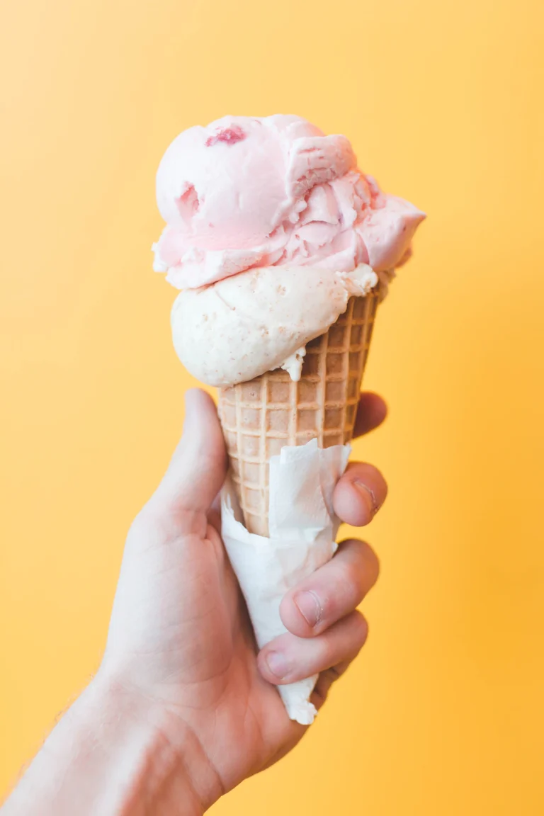 Hand holding a soft serve ice cream cone against a yellow background