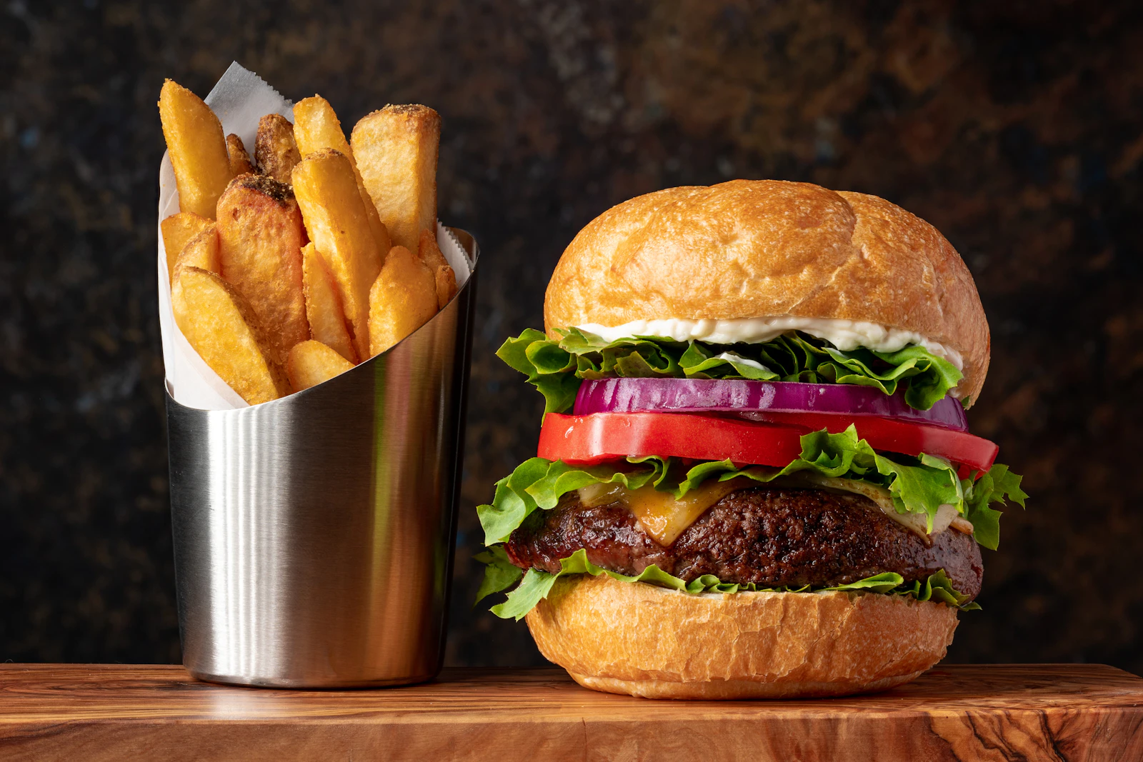 Cheeseburger with a cup of golden fries on a wooden board