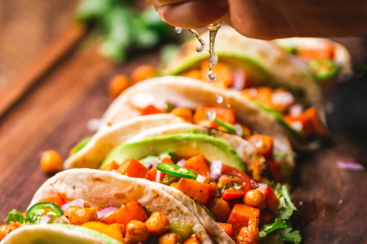 Row of tacos topped with fresh salsa and herbs
